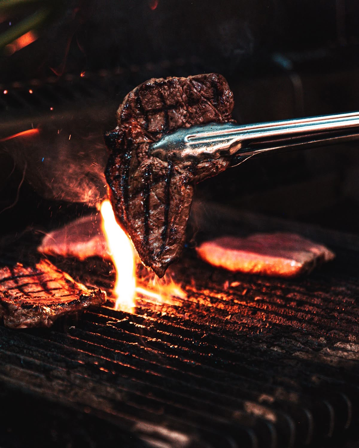 Grilled steak held above the fire with tongs
