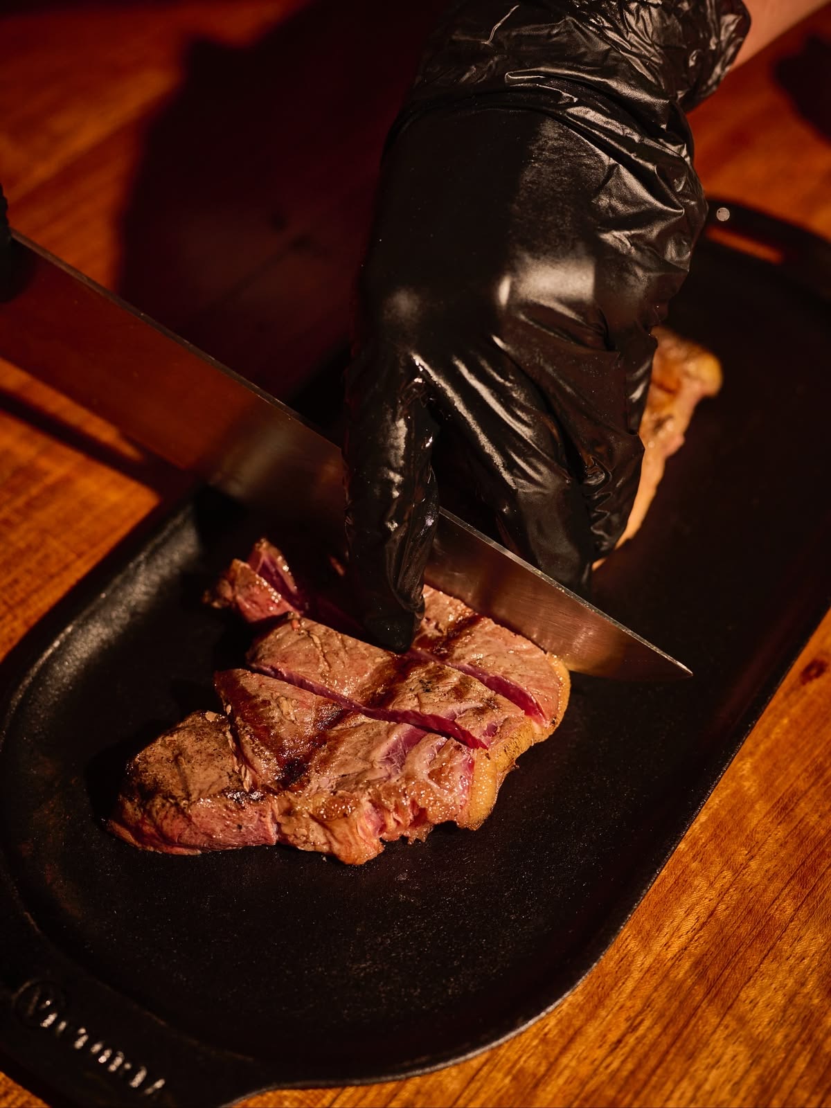 A chef slicing a rested steak on a cast iron plate